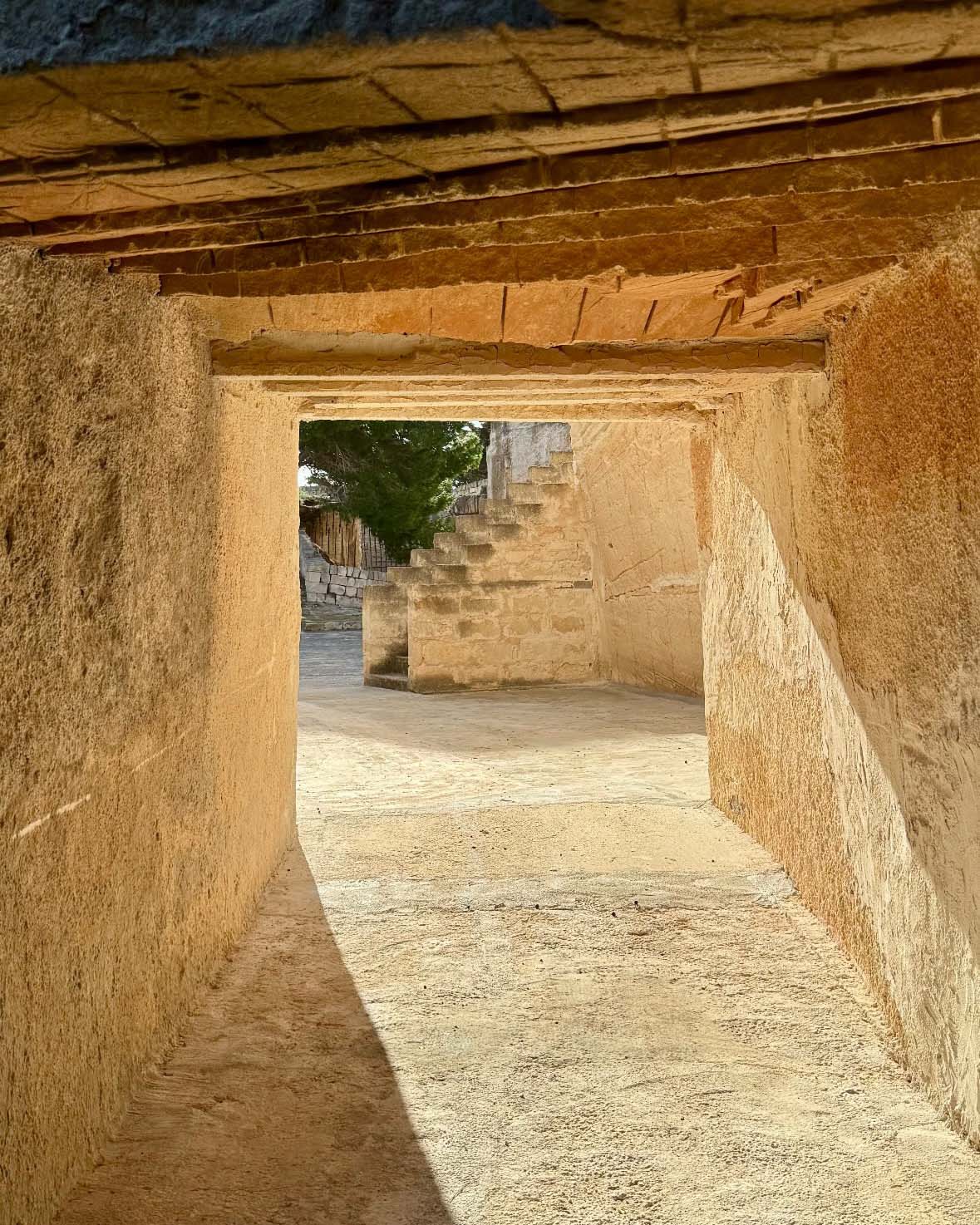 Passaggio nella cava di tufo di Mae a Favignana con pareti in pietra, luce naturale e scala visibile sul fondo.