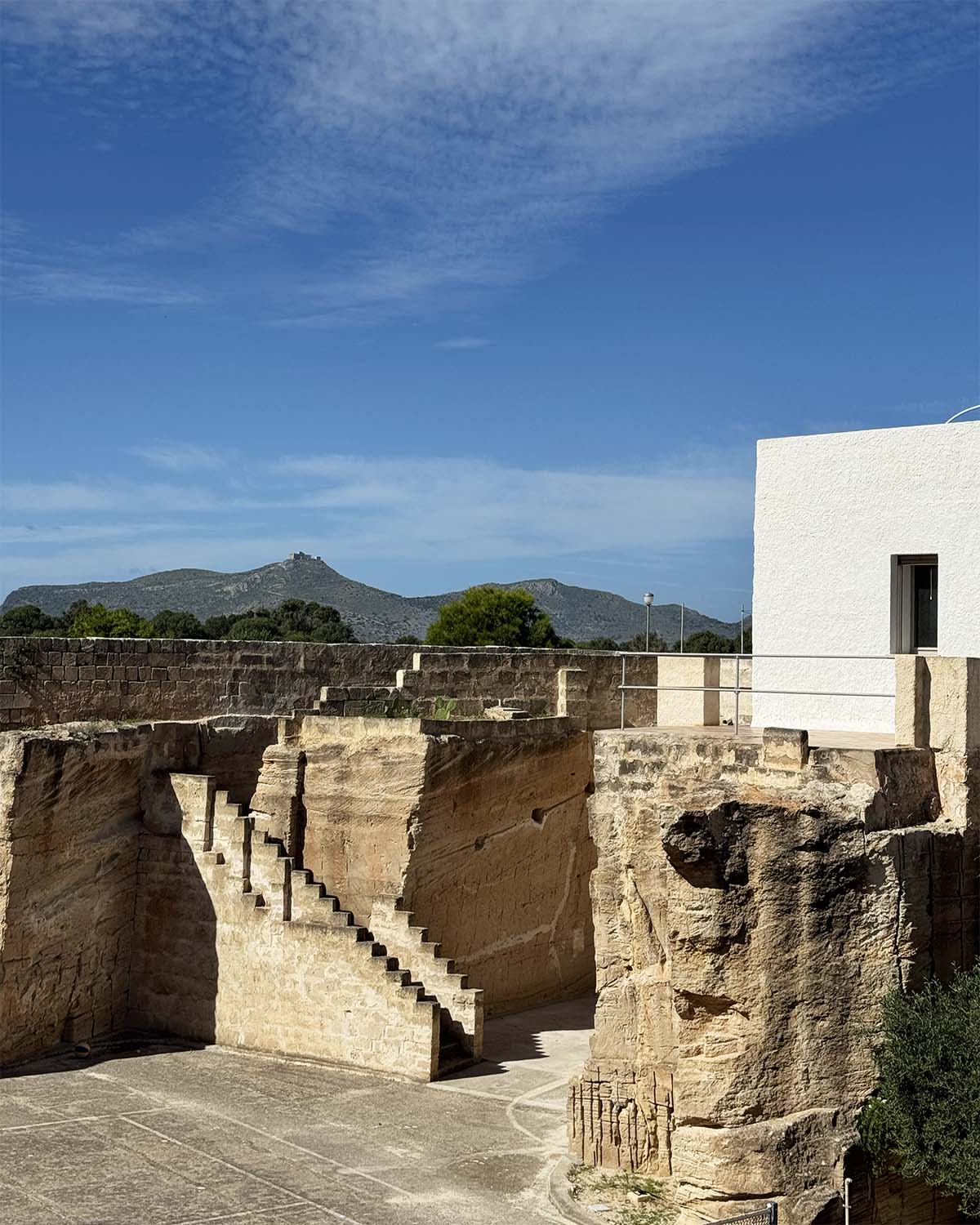 Vista della residenza Mae a Favignana affacciata sulla cava di tufo, con scale scavate nella pietra e profilo del paesaggio sullo sfondo.